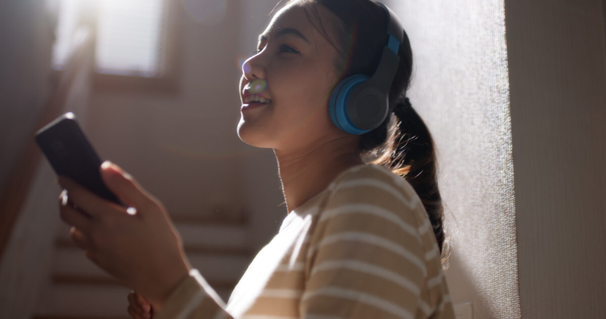 Une femme écoute un podcast avec des écouteurs tout en tenant son téléphone dans ses mains.