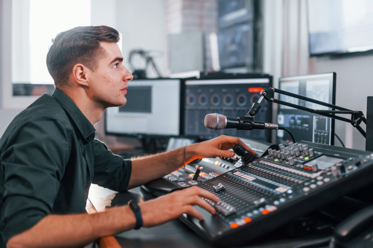 Un technicien supervise l'enregistrement d'un podcast derrière un mixeur audio.