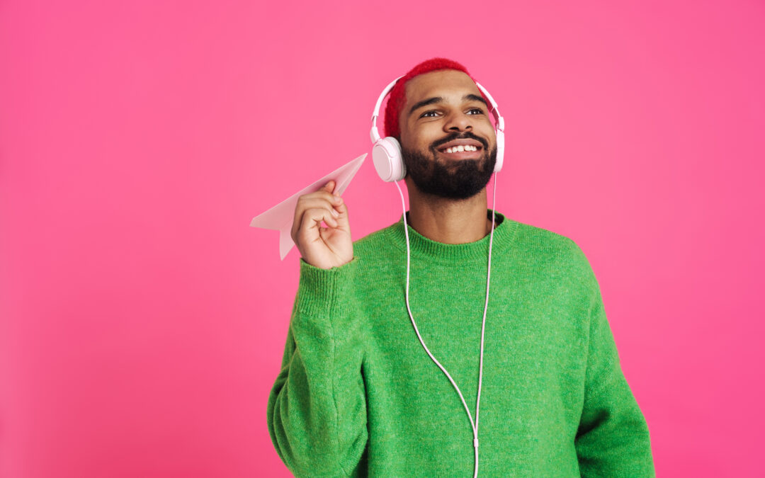 Un homme portant un chandail vert écoute un podcast héberger sur Apple Balados devant un mur rose